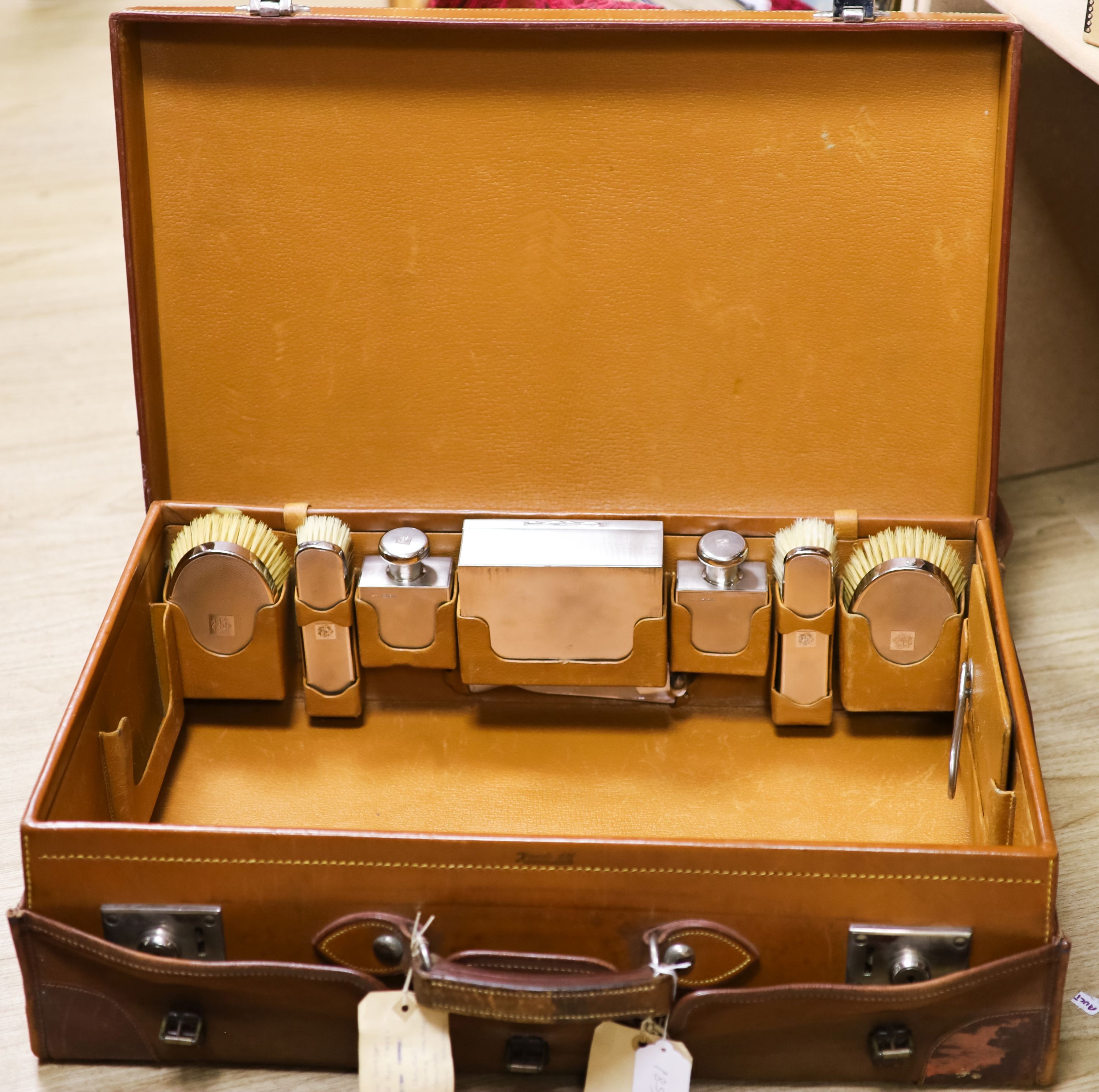 A 1930's Harrods pigskin travelling toilet case with seven engine turned silver fittings, including brushes, cigarette box and two scent bottles, F & Co Ltd, London, 1933, case 66.5cm.